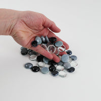 Video of white-black-grey mix glass nuggets in black, grey, white and clear shades with an iridescent sheen, 16–20 mm, picked up from a pile by hand and dropped back to show their size, round shape and shine